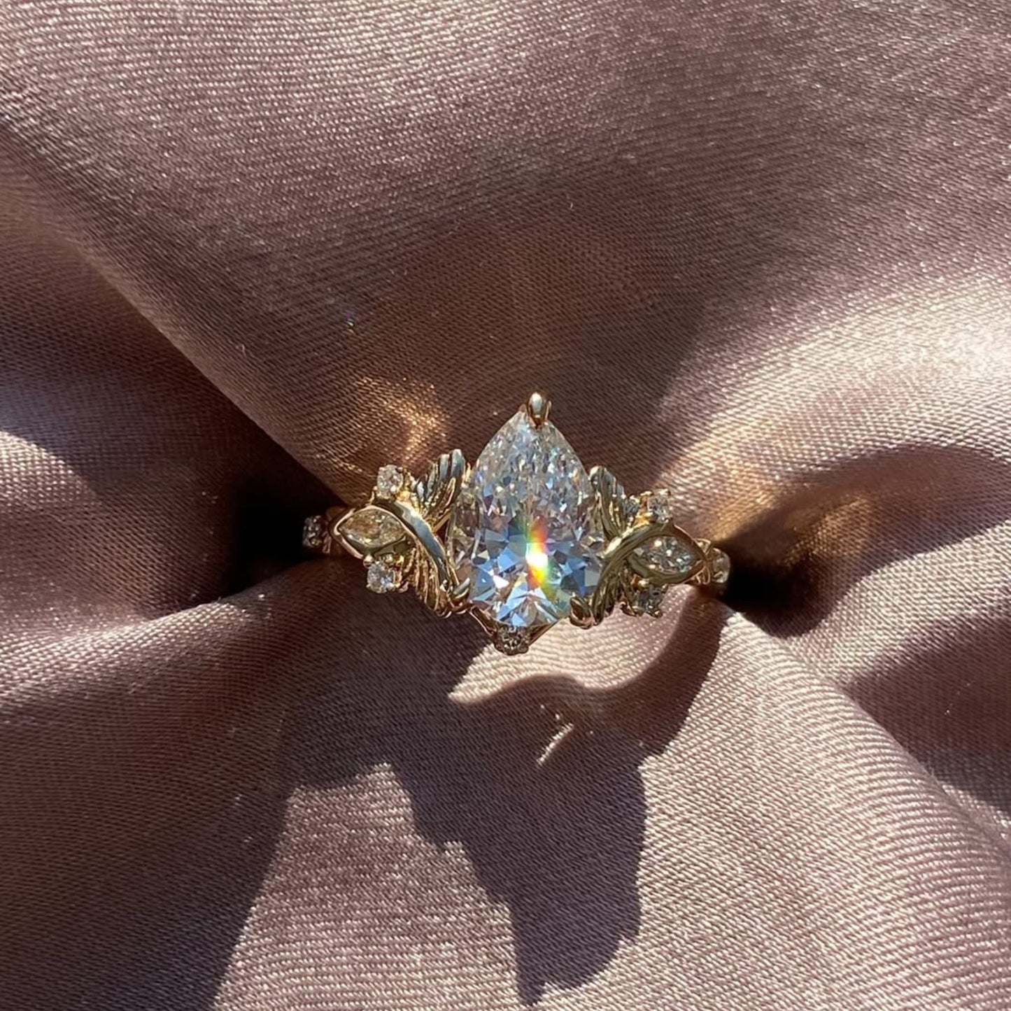 vintage inspired pear cut moissanite diamond engagement ring with floral leaf side accents in solid gold