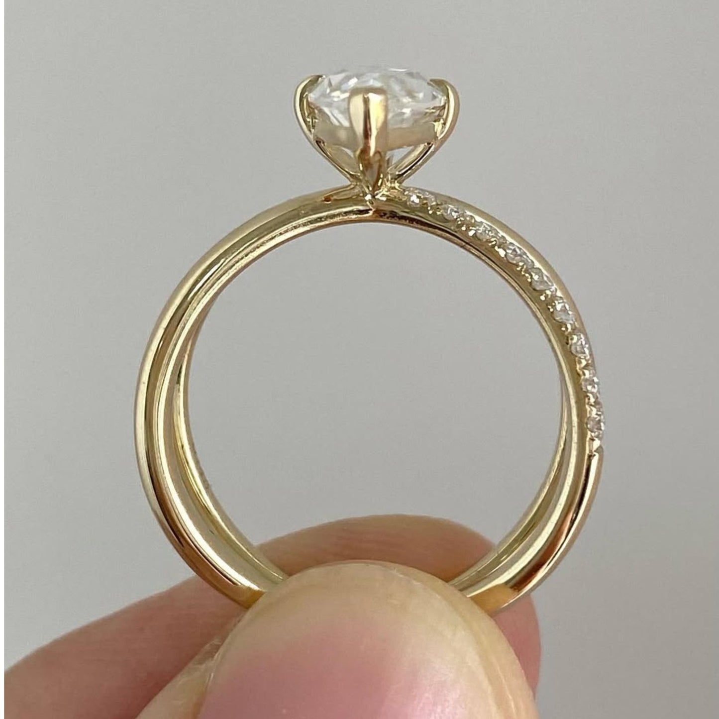 gold ring with a diamond held between fingers against a neutral background