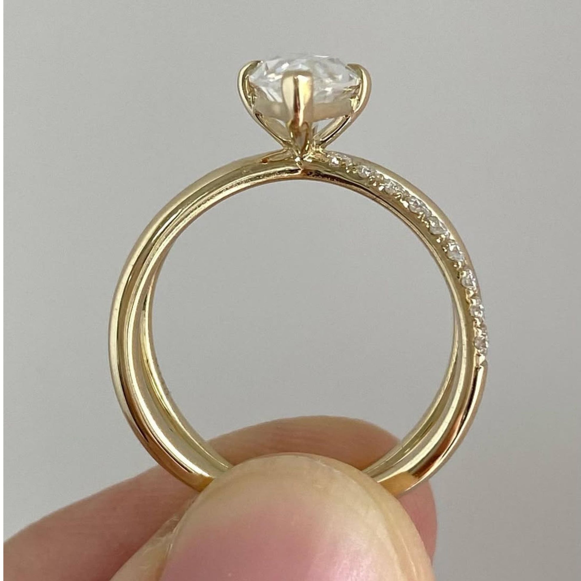 Gold ring with a diamond held between fingers against a neutral background