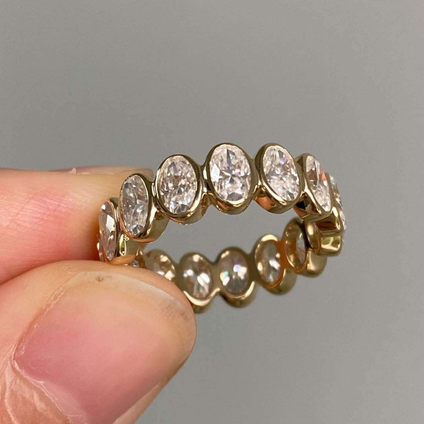 gold ring with diamonds held between fingers against a gray background