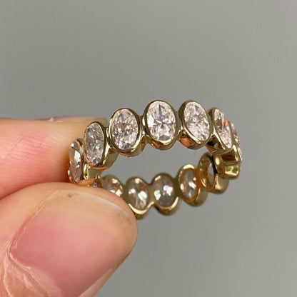 Gold ring with diamonds held between fingers against a gray background