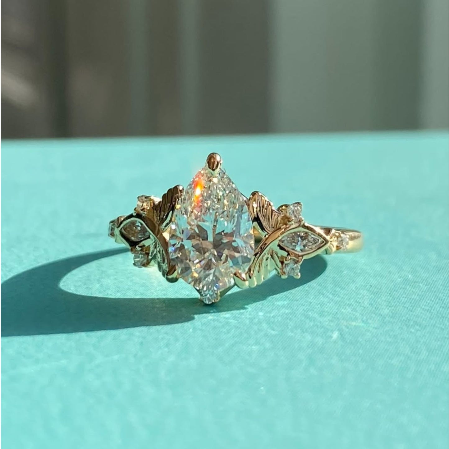 vintage inspired pear cut moissanite diamond engagement ring with floral leaf side accents in solid gold
