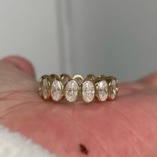 Gold ring with large diamonds on a hand against a neutral background