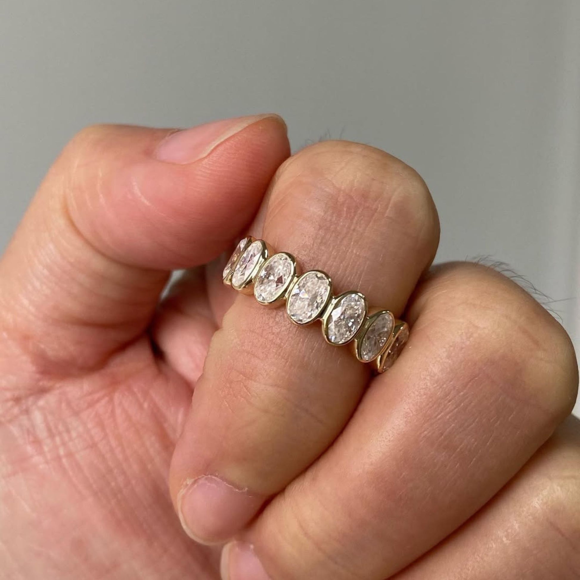 Gold ring with oval-shaped diamonds on a hand against a neutral background