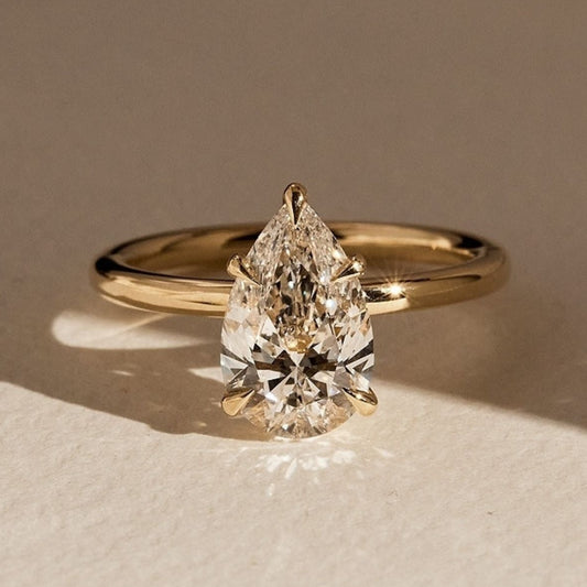 Gold ring with a pear-shaped diamond on a beige surface