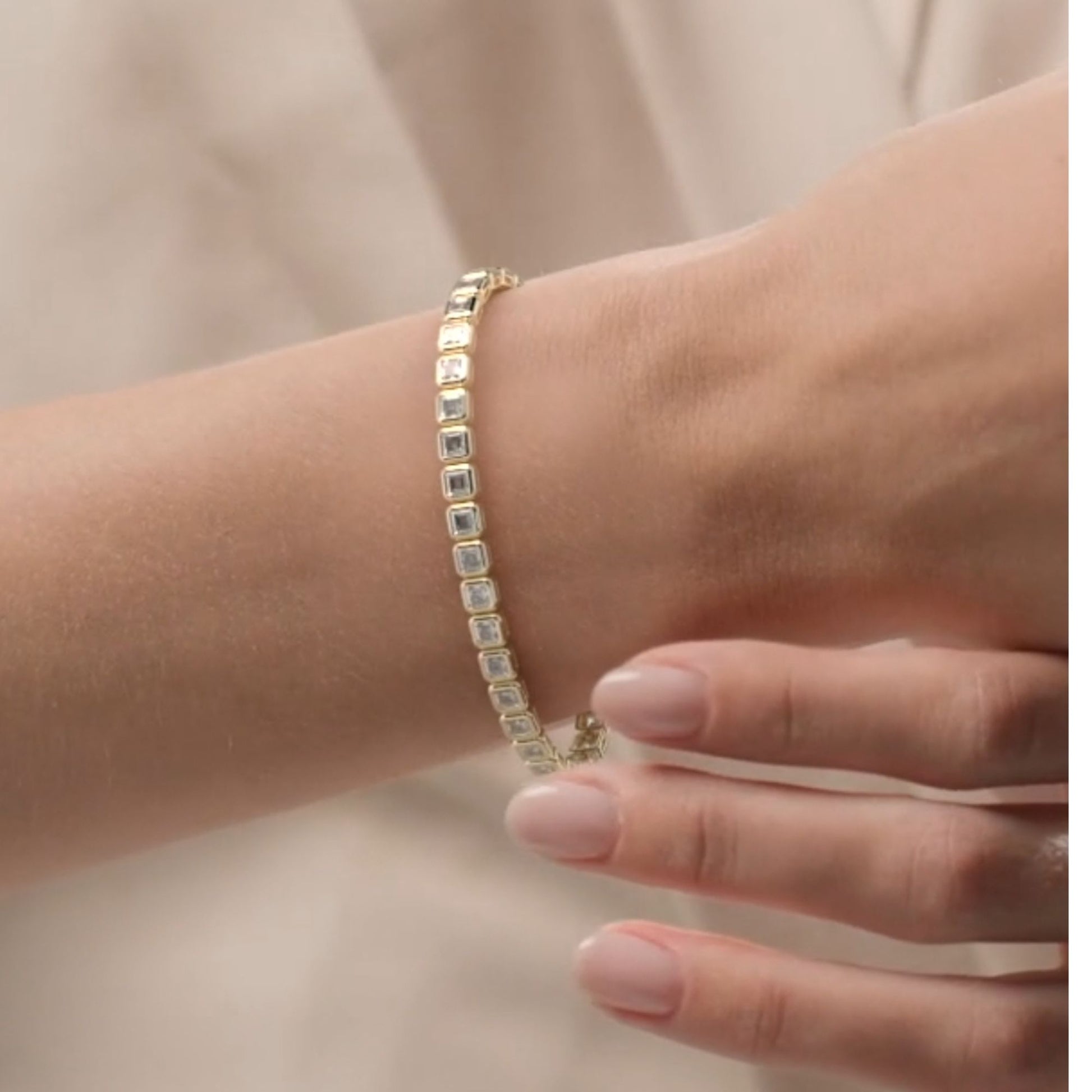 Gold bracelet with square-cut stones on a wrist against a neutral background