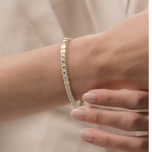 Gold bracelet with square-cut stones on a wrist against a neutral background