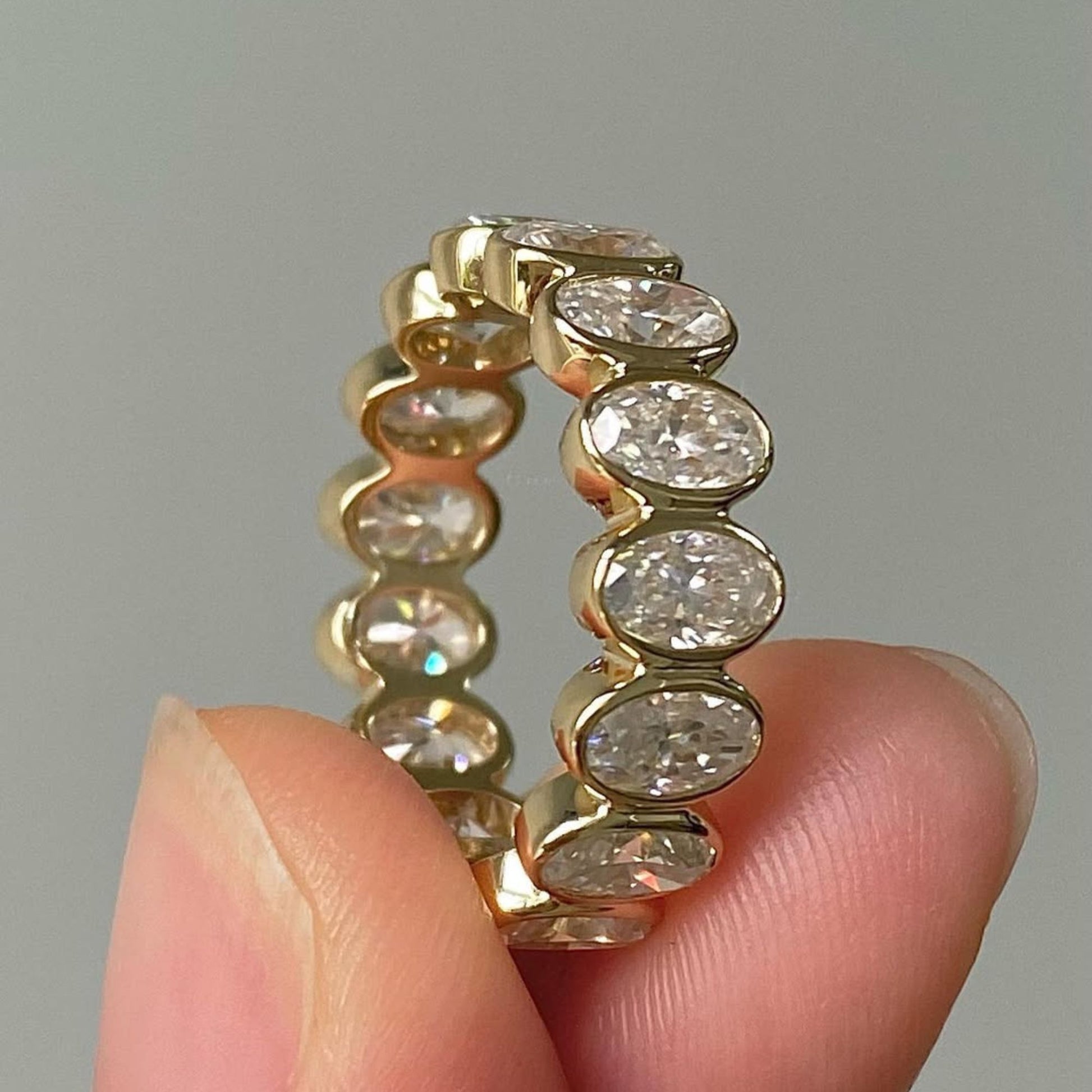 Gold ring with diamonds held between fingers against a neutral background
