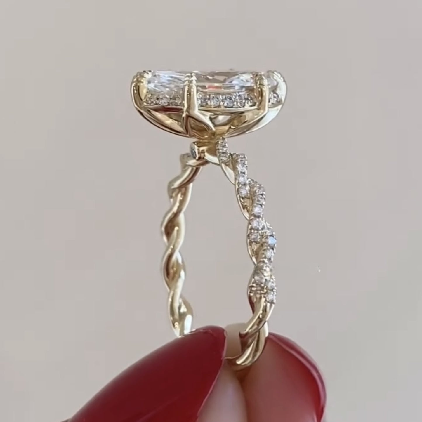 gold ring with diamond accents held by a hand with red nail polish on a neutral 