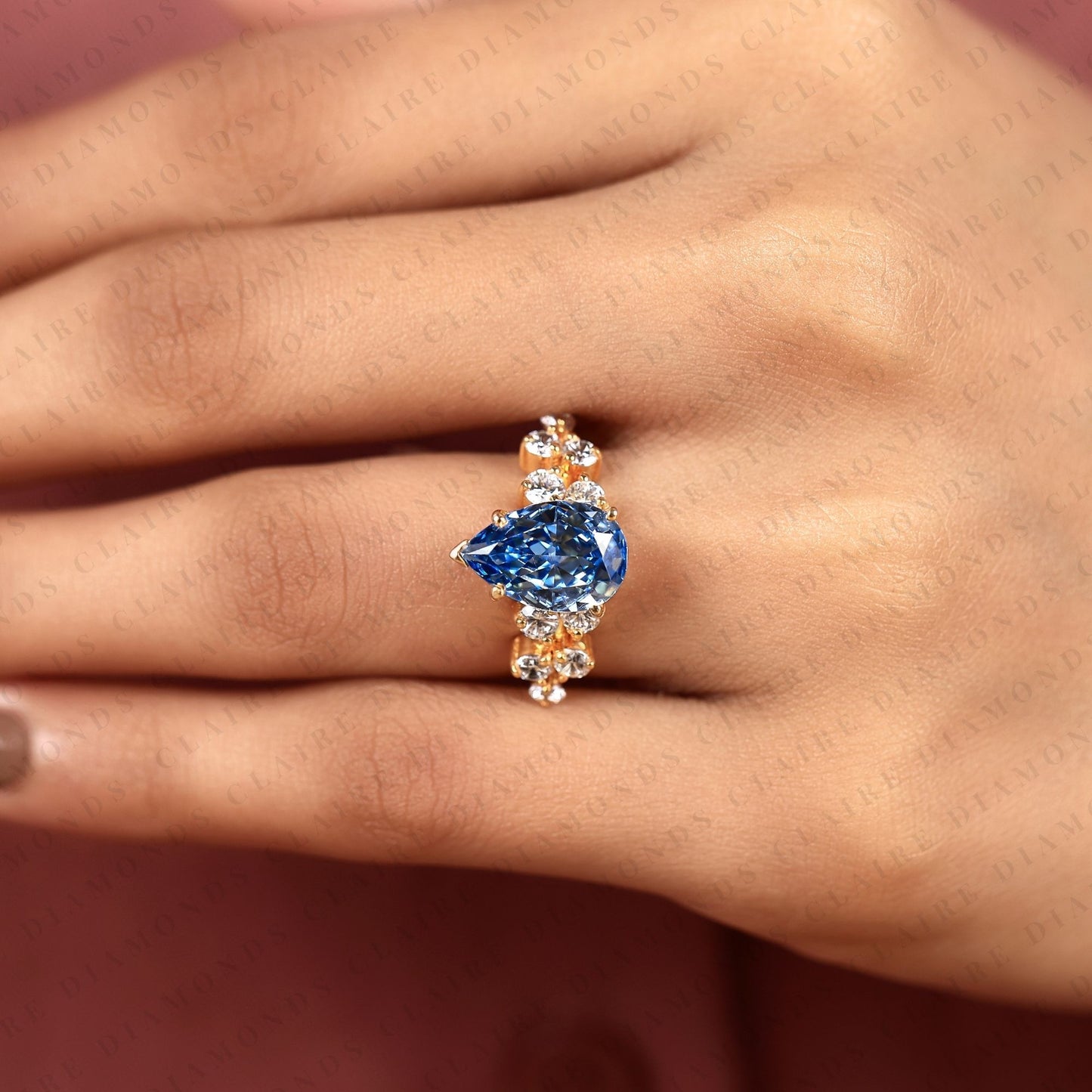 pear cut blue lab grown engagement ring, round diamond floral side stones, yellow gold nature-inspired bridal ring