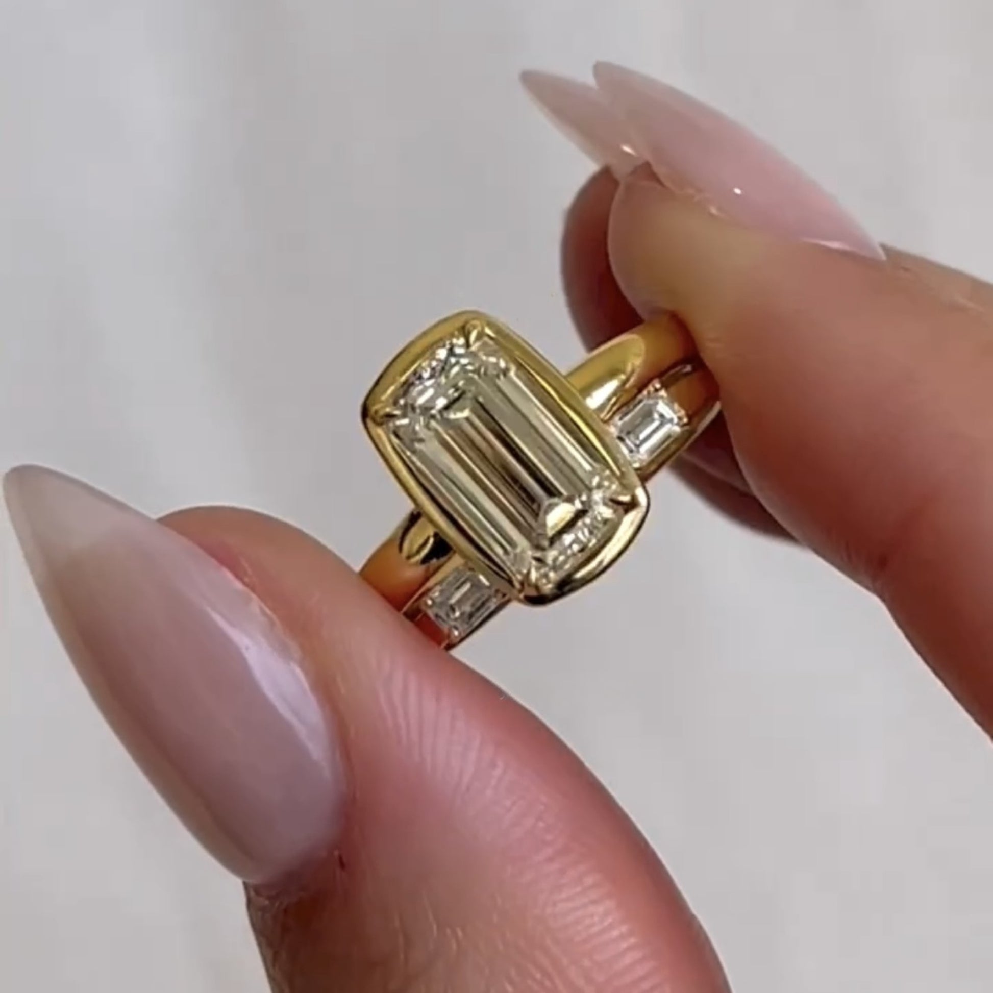 Gold ring with a large diamond held between fingers against a white 