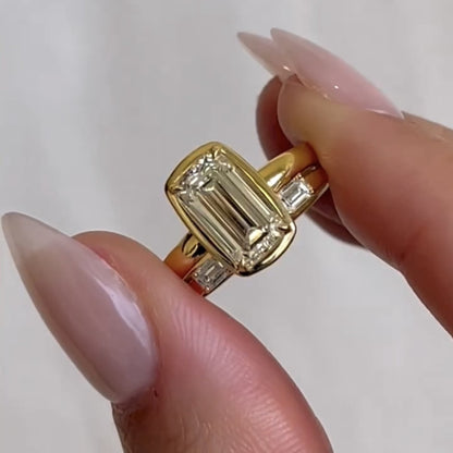 Gold ring with a large diamond held between fingers against a white 