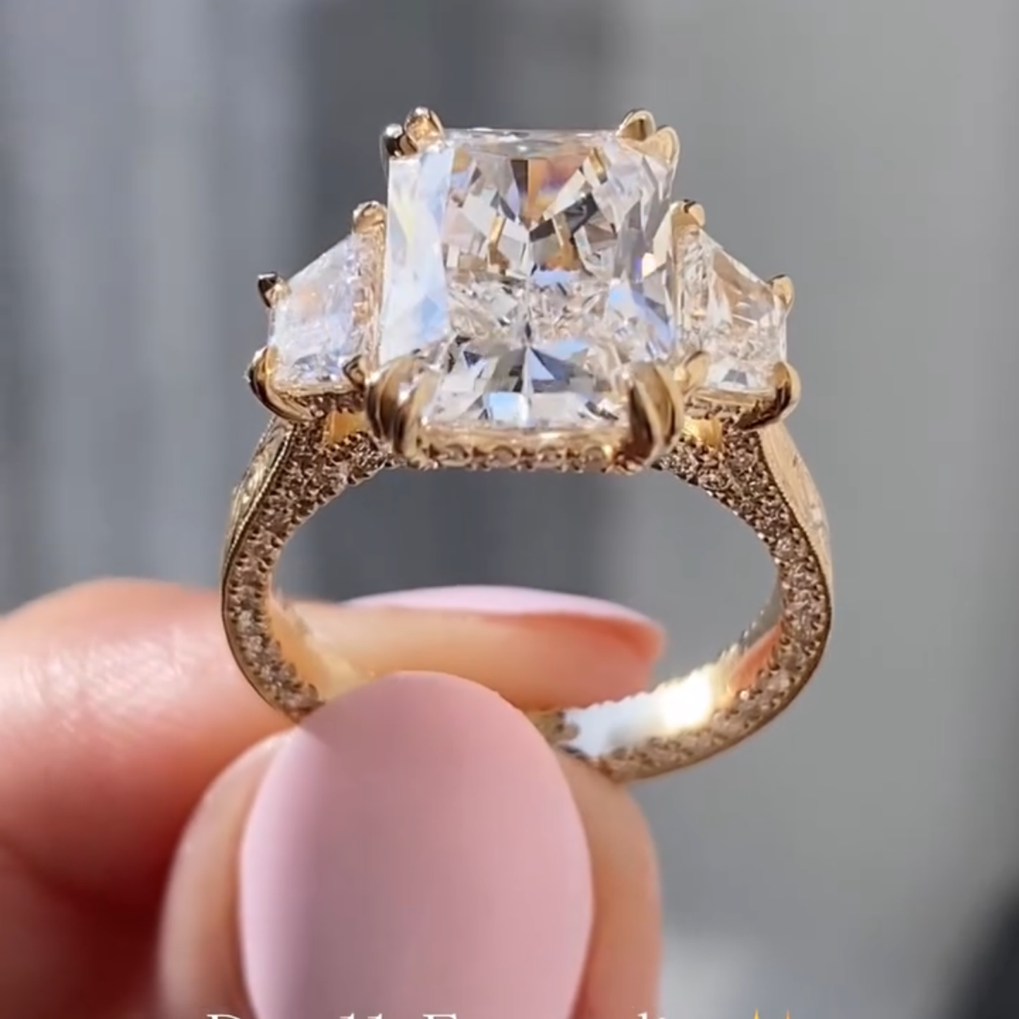 gold ring with large diamond held by a hand against a blurred 