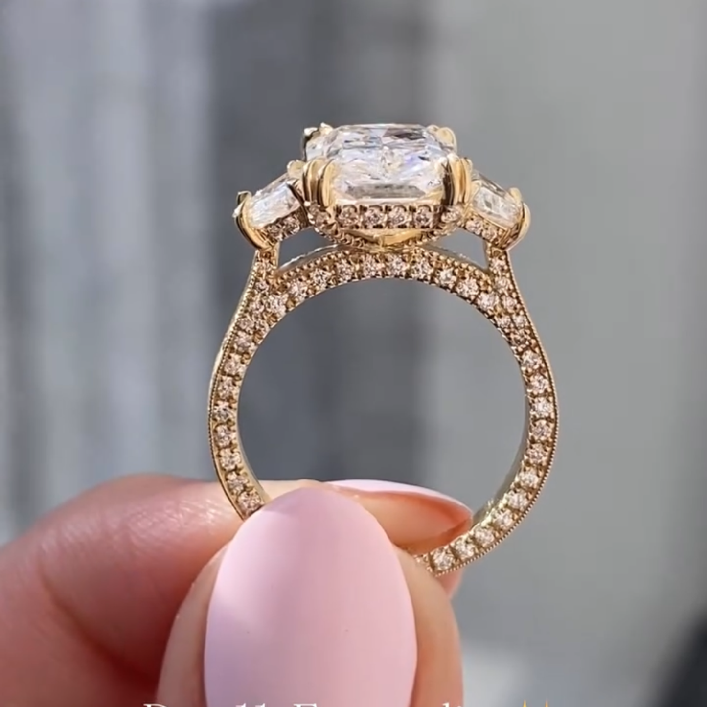 gold ring with a large diamond held by a hand against a blurred background