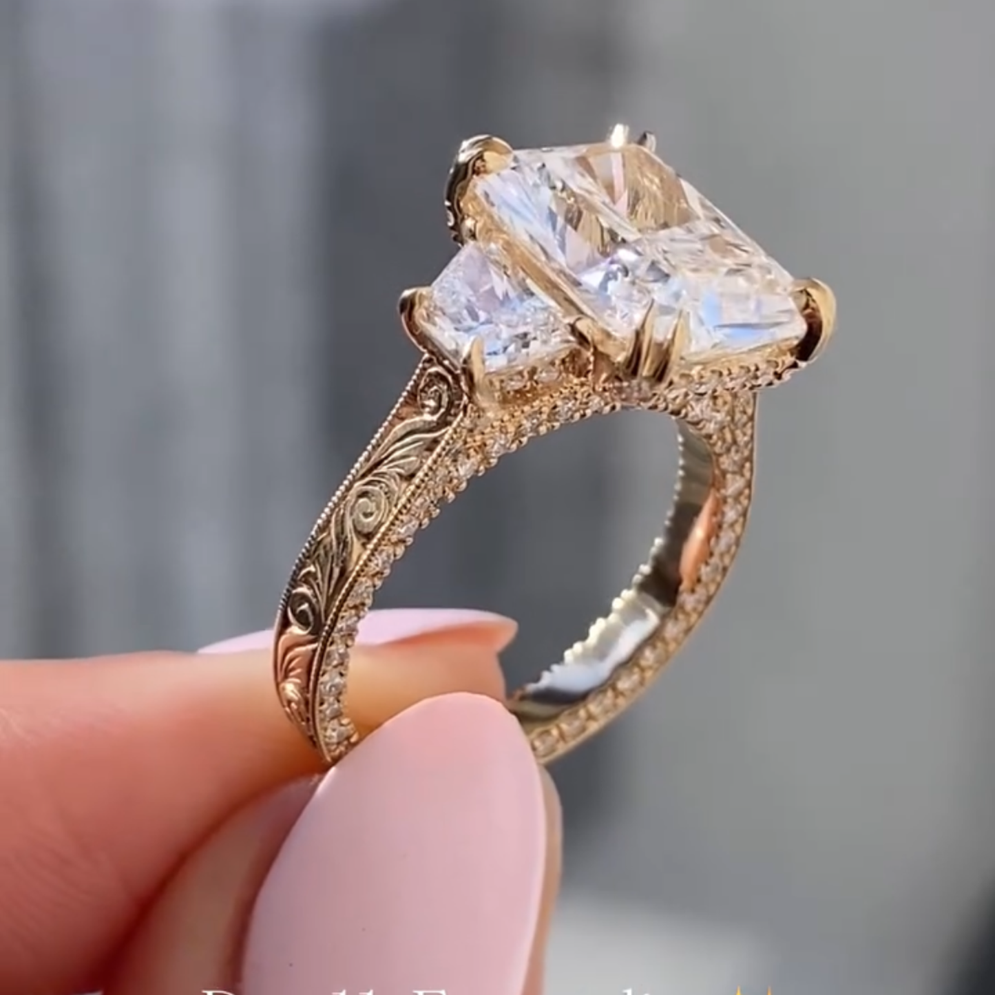 gold ring with a large diamond held by a hand against a gray 