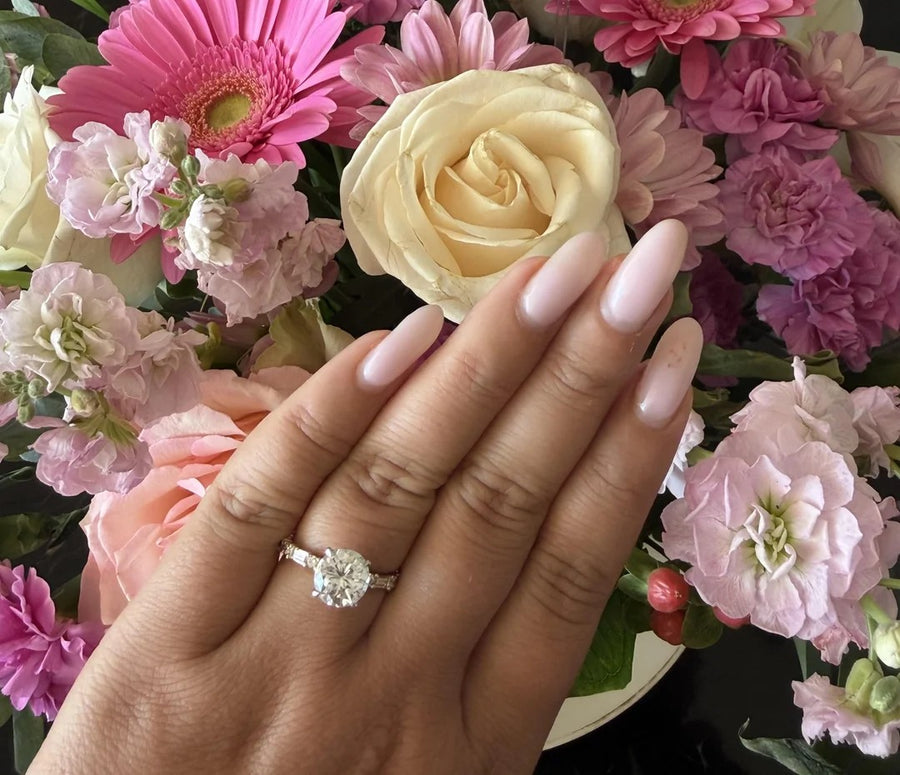 Round diamond ring on a hand over pink and cream flowers