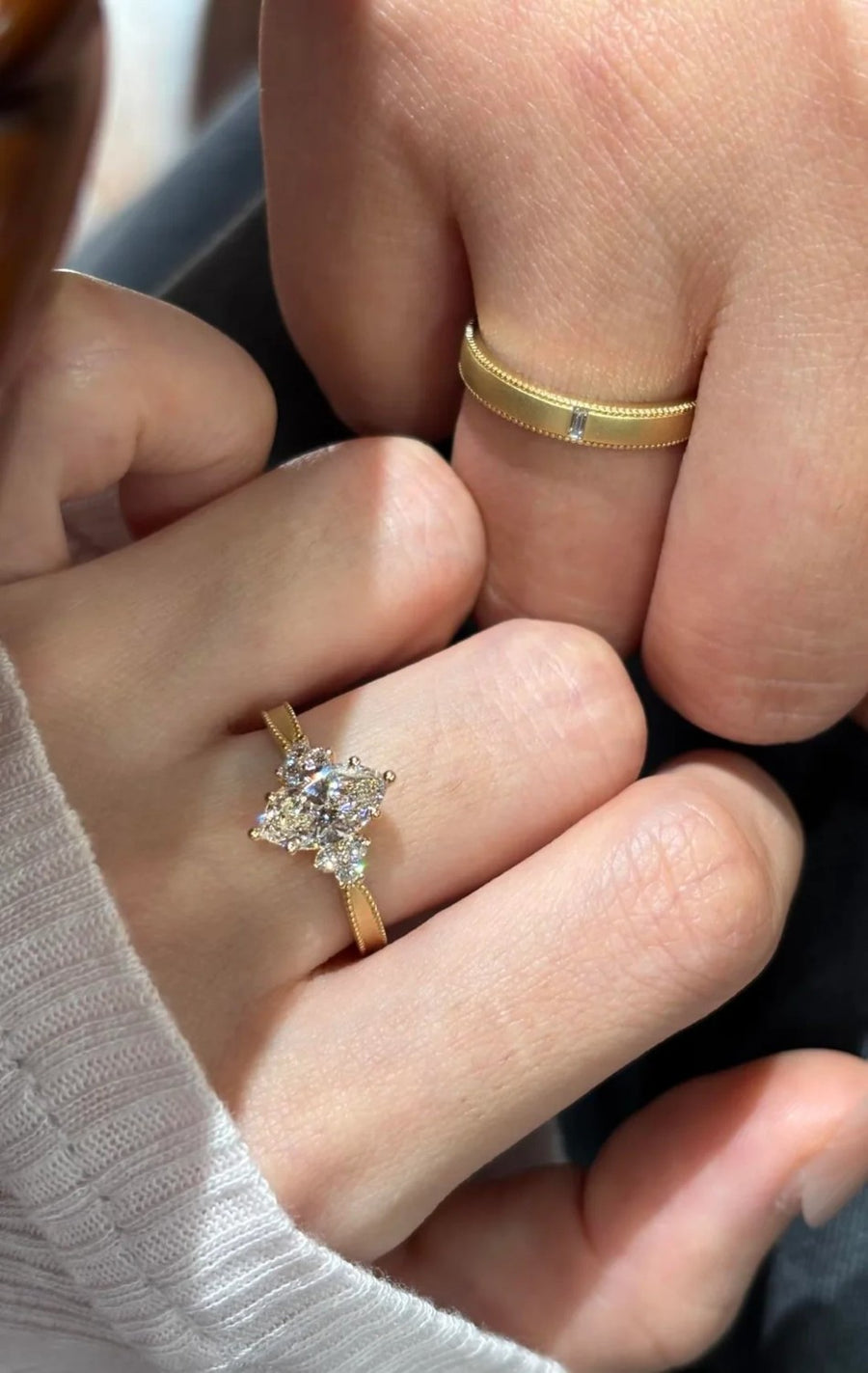 Cluster engagement ring and matte gold wedding band on two hands