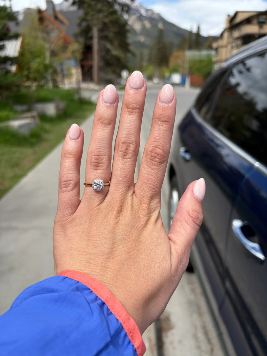 Round halo ring on a yellow gold band, hand held up outdoors