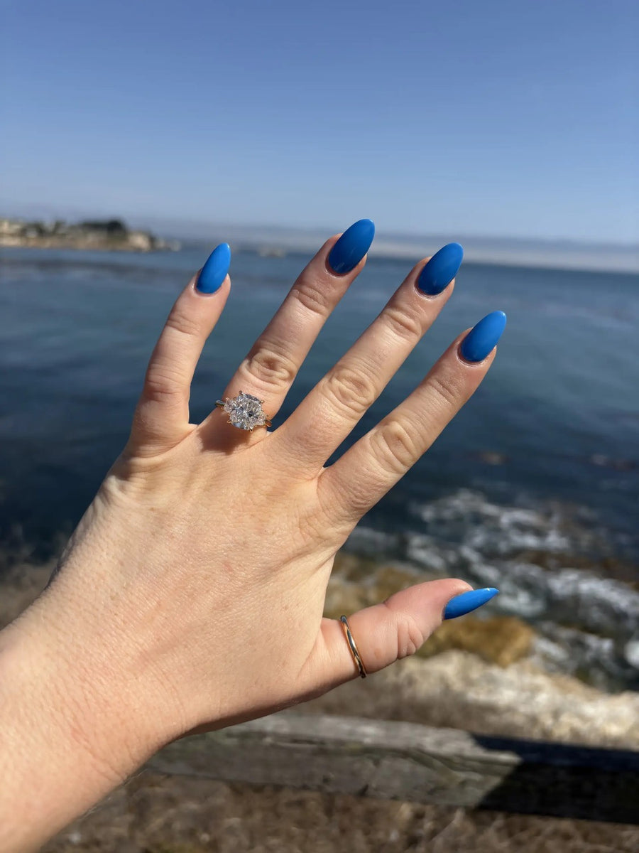 Diamond ring on a hand held up against the ocean