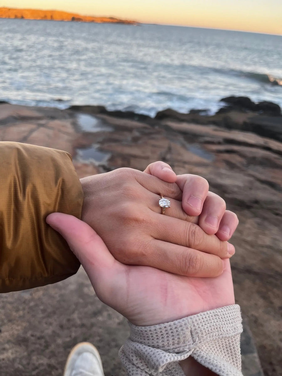 Solitaire ring on clasped hands by the sea at sunset