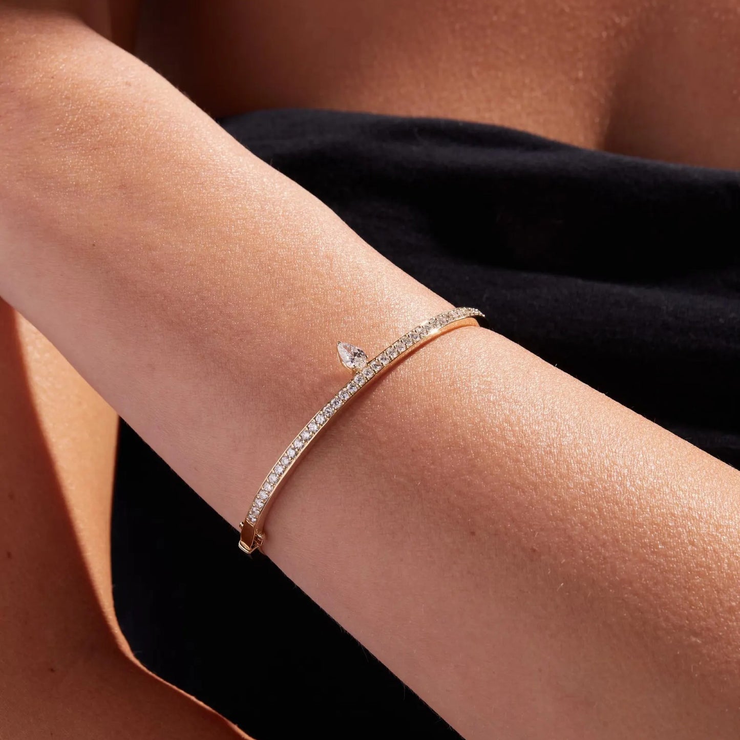 rose gold bracelet with diamonds on a person's wrist against a black 