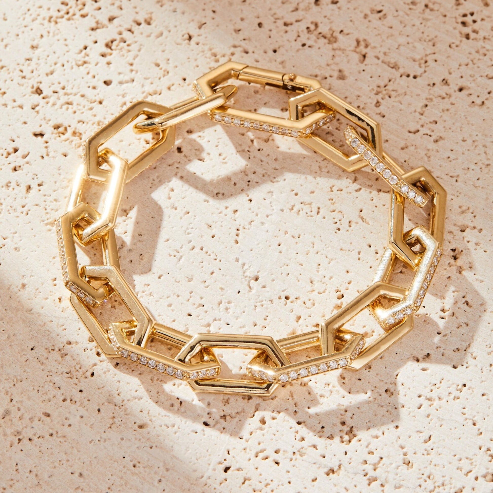 Gold chain bracelet with diamond accents on a textured beige surface
