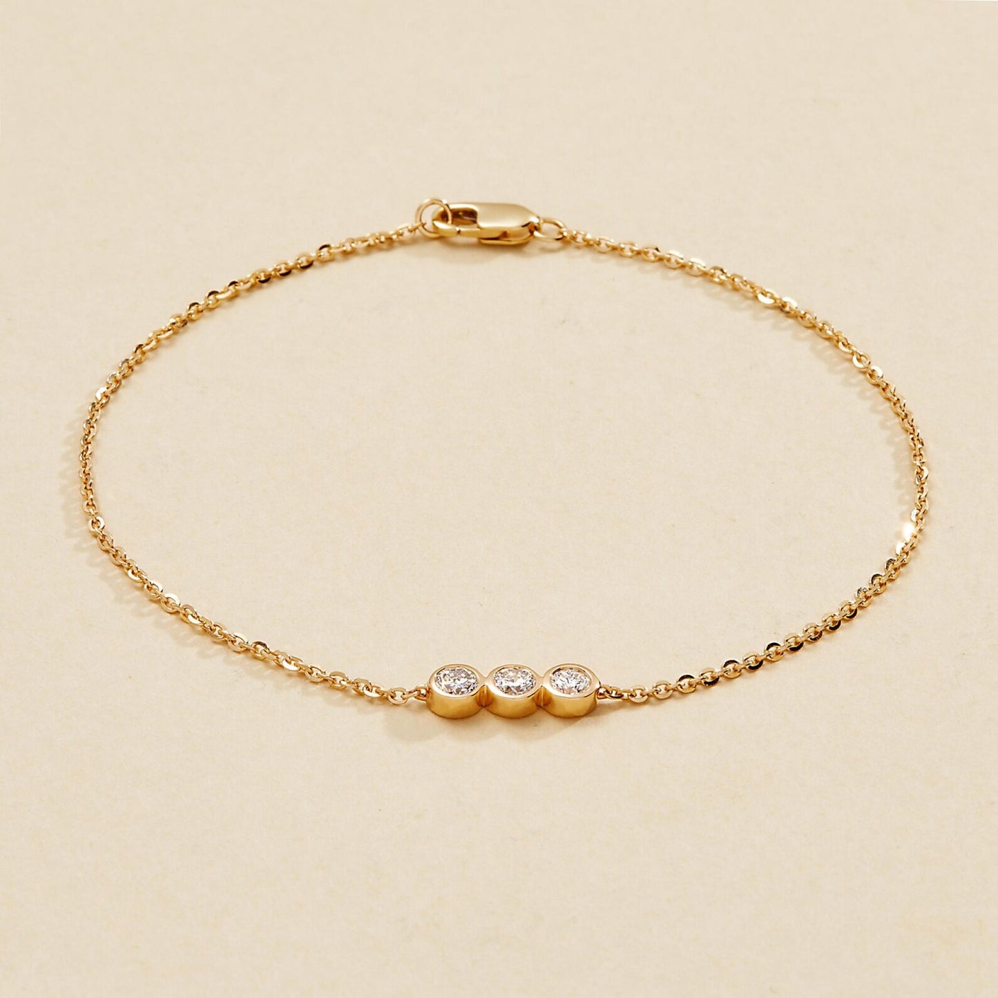 gold bracelet with three small round diamonds on a beige 