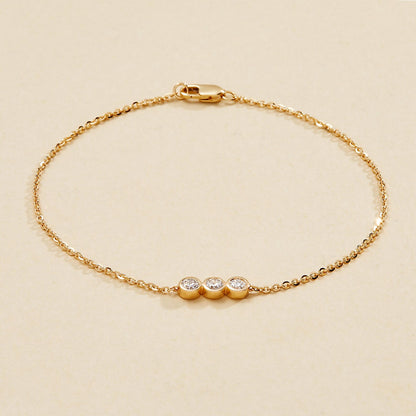 Gold bracelet with three small round diamonds on a beige 