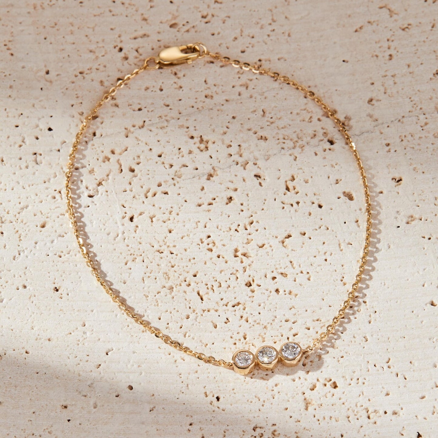 gold bracelet with three clear stones on a textured beige surface
