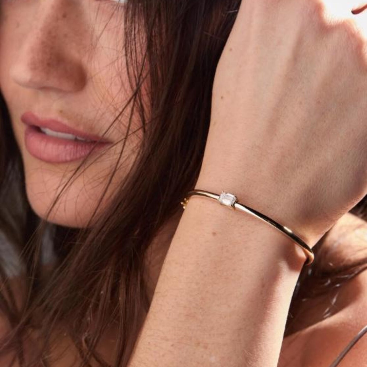 close-up of a woman's hand wearing a gold bracelet with a diamond on a blurred 