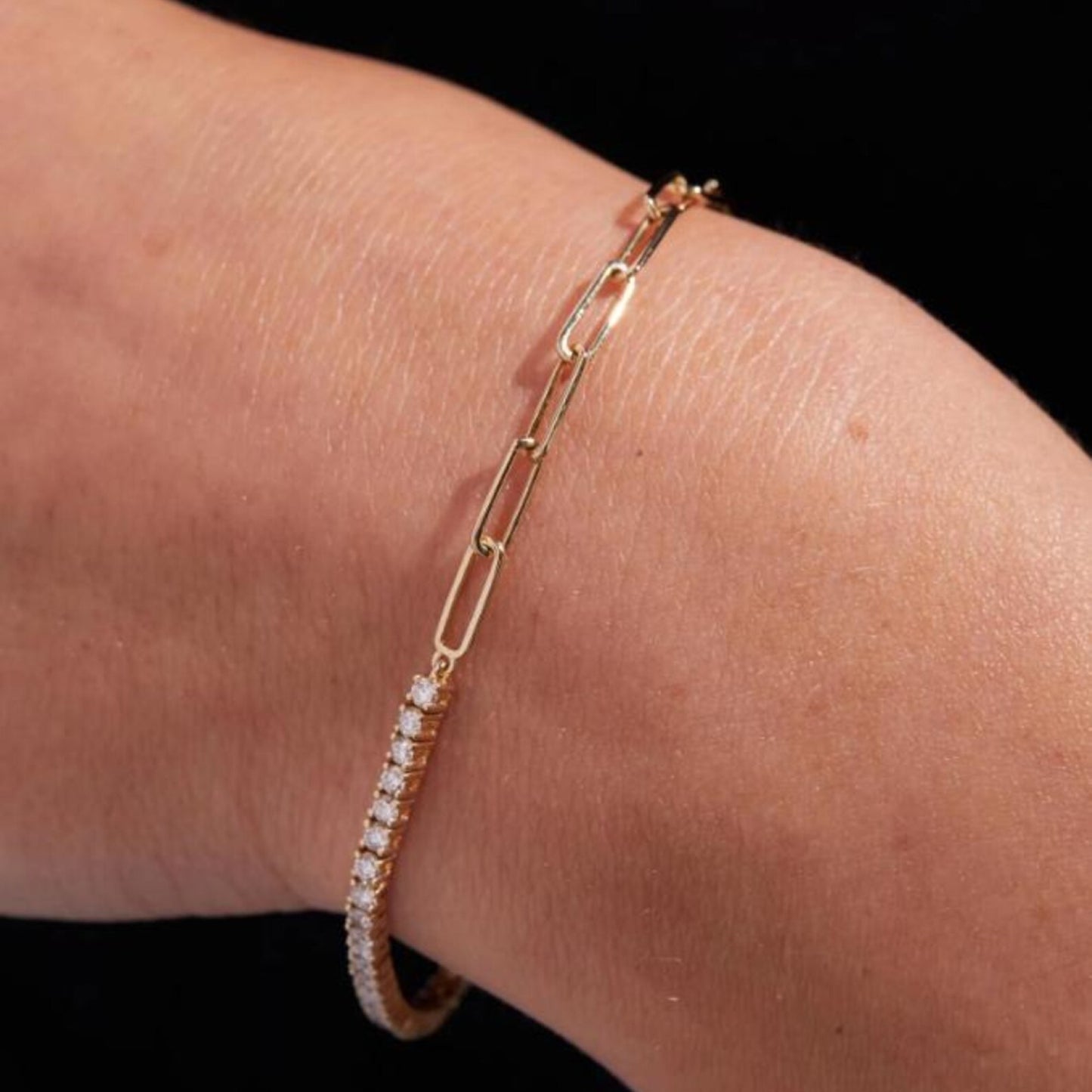 gold bracelet with clear stones on a wrist against a black 