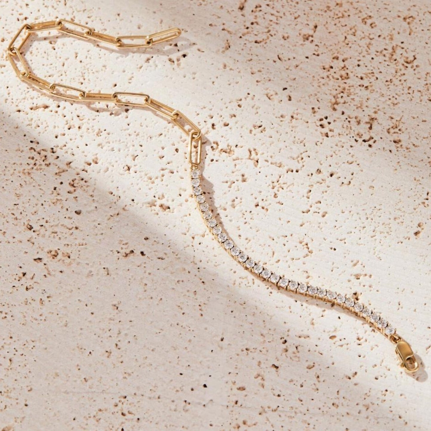 gold bracelet with clear stones on a textured beige surface