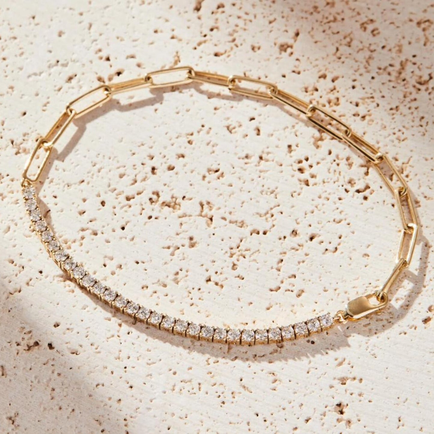 gold bracelet with clear stones on a textured beige surface