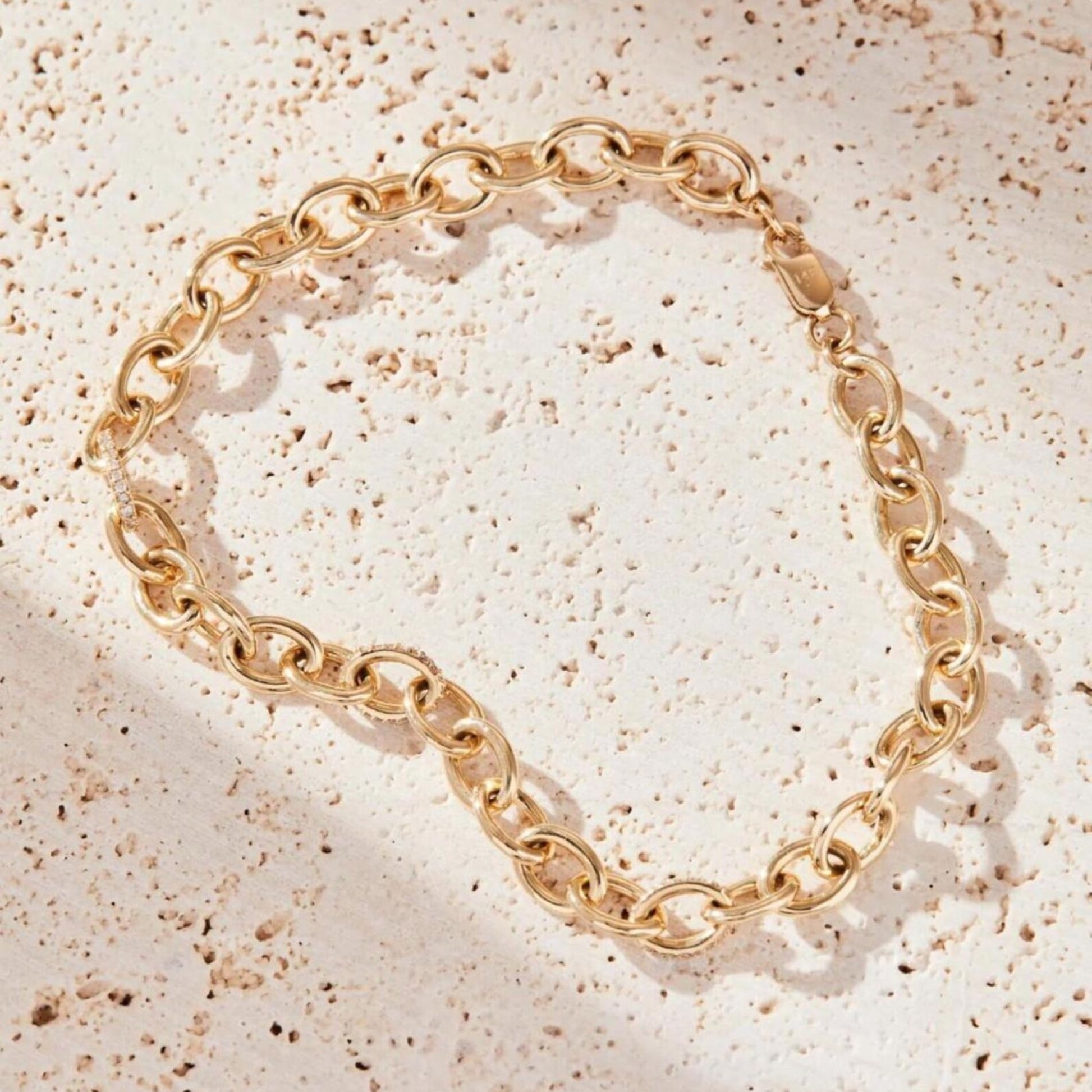 Gold chain bracelet on a textured beige surface