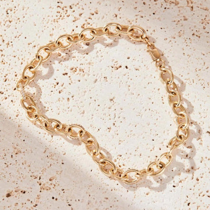 Gold chain bracelet on a textured beige surface